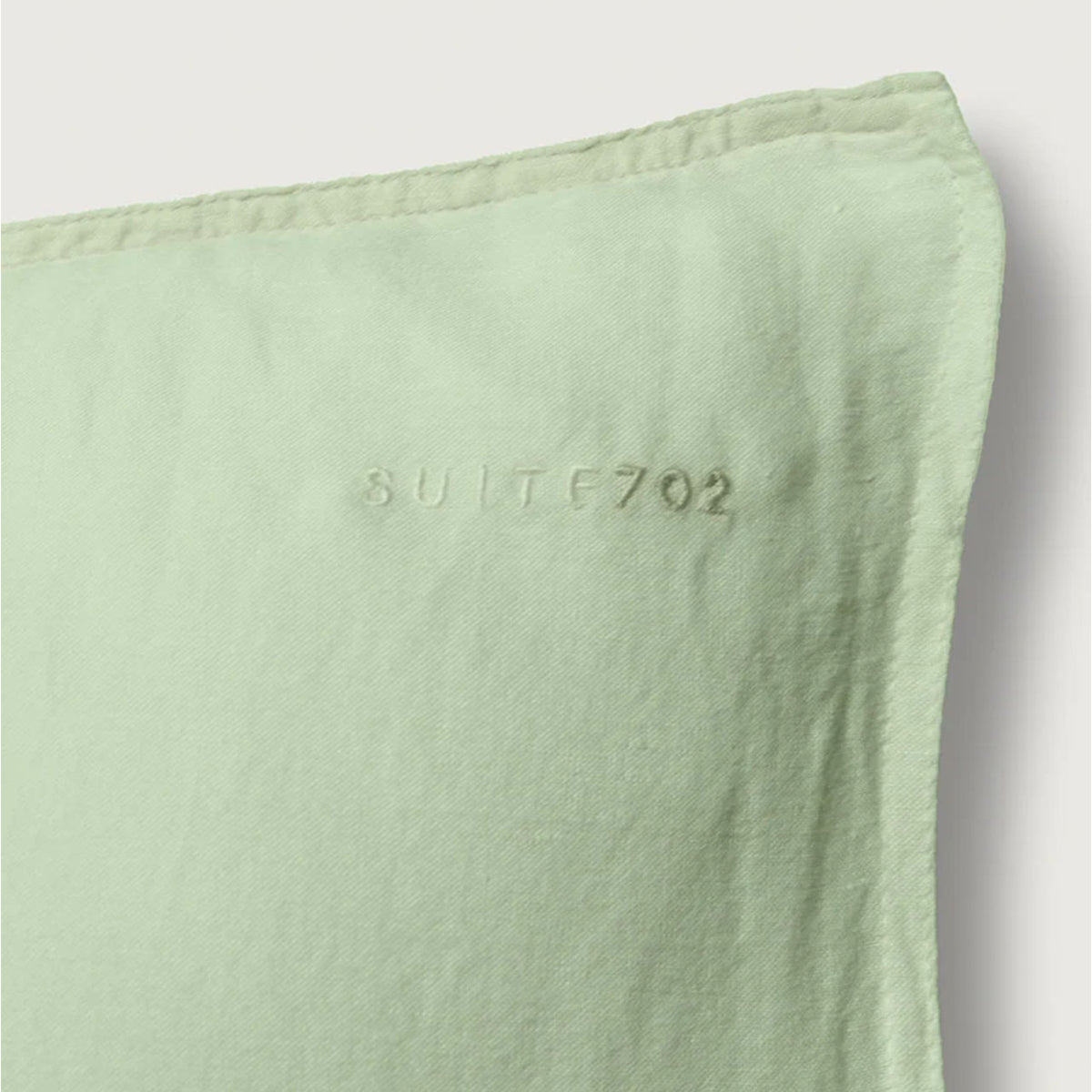 Nahaufnahme der Ecke des Suite702 Leinen-Mix Kissenbezugs in Green Mint mit eingeprägtem „Suite702“-Schriftzug