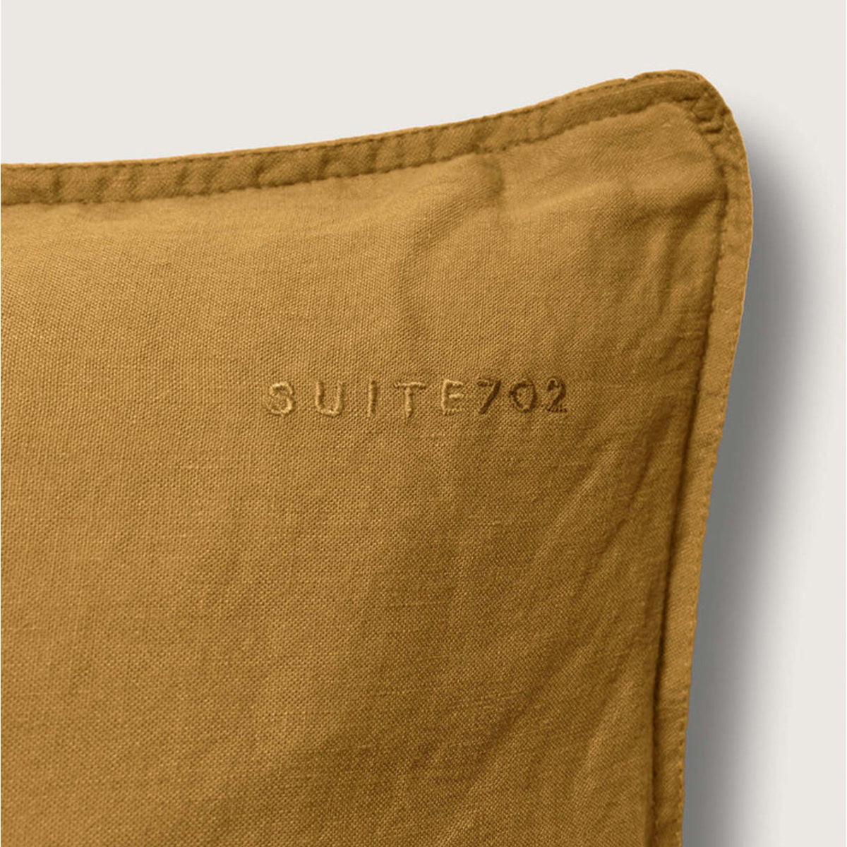 Nahaufnahme der Ecke des Suite702 Leinen-Mix Kissenbezugs in Khaki Gold mit eingesticktem „Suite702“-Schriftzug