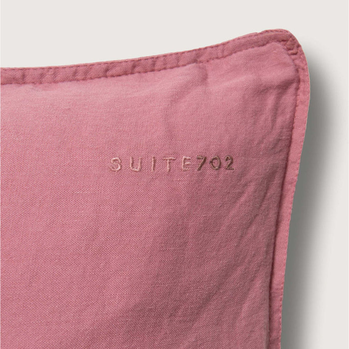 Nahaufnahme der Eckennaht des Suite702 Leinen-Mix Kissenbezugs in Mauve Rose mit eingesticktem „Suite702“-Schriftzug