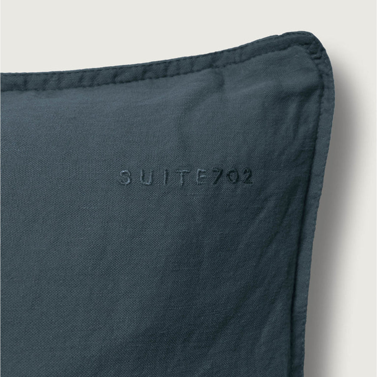 Nahaufnahme der Ecke eines Suite702 Leinen-Mix Kissenbezugs in Midnight Blue mit eingesticktem „Suite702“-Schriftzug