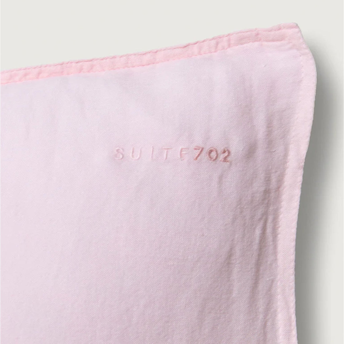 Nahaufnahme der Ecke des Suite702 Leinen-Mix Kissenbezugs in Shell Pink mit eingewebtem Schriftzug „Suite702“