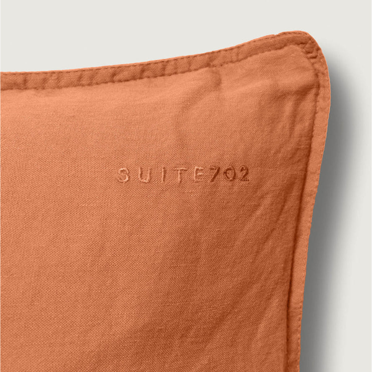 Nahaufnahme der Eckennaht des Suite702 Leinen-Mix Kissenbezugs in Terra mit eingesticktem „Suite702“-Schriftzug