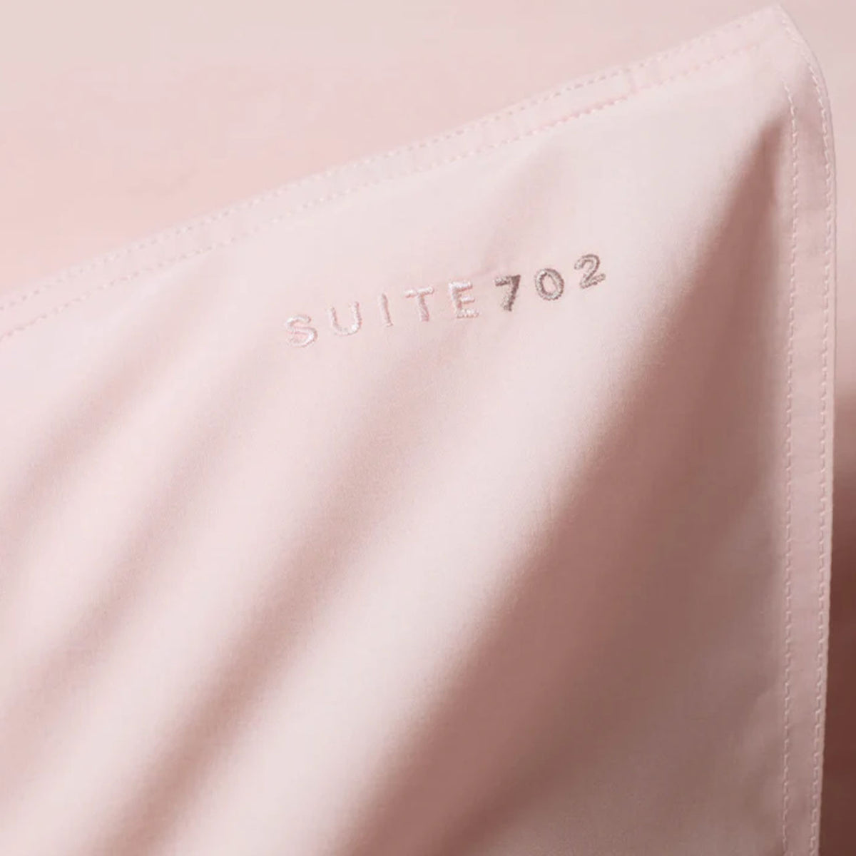 Nahaufnahme der eingestickten „Suite702“-Schriftzugs auf rosa Perkal-Kissenbezug