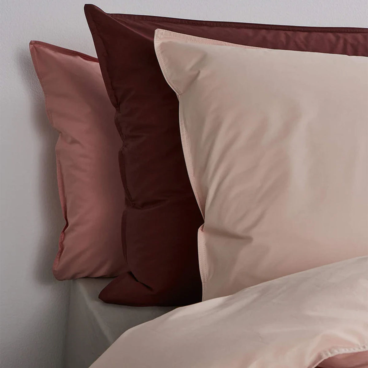 Suite702 Perkal-Kissenbezüge in Altrosa, Weinrot und Beige nebeneinander am Bett