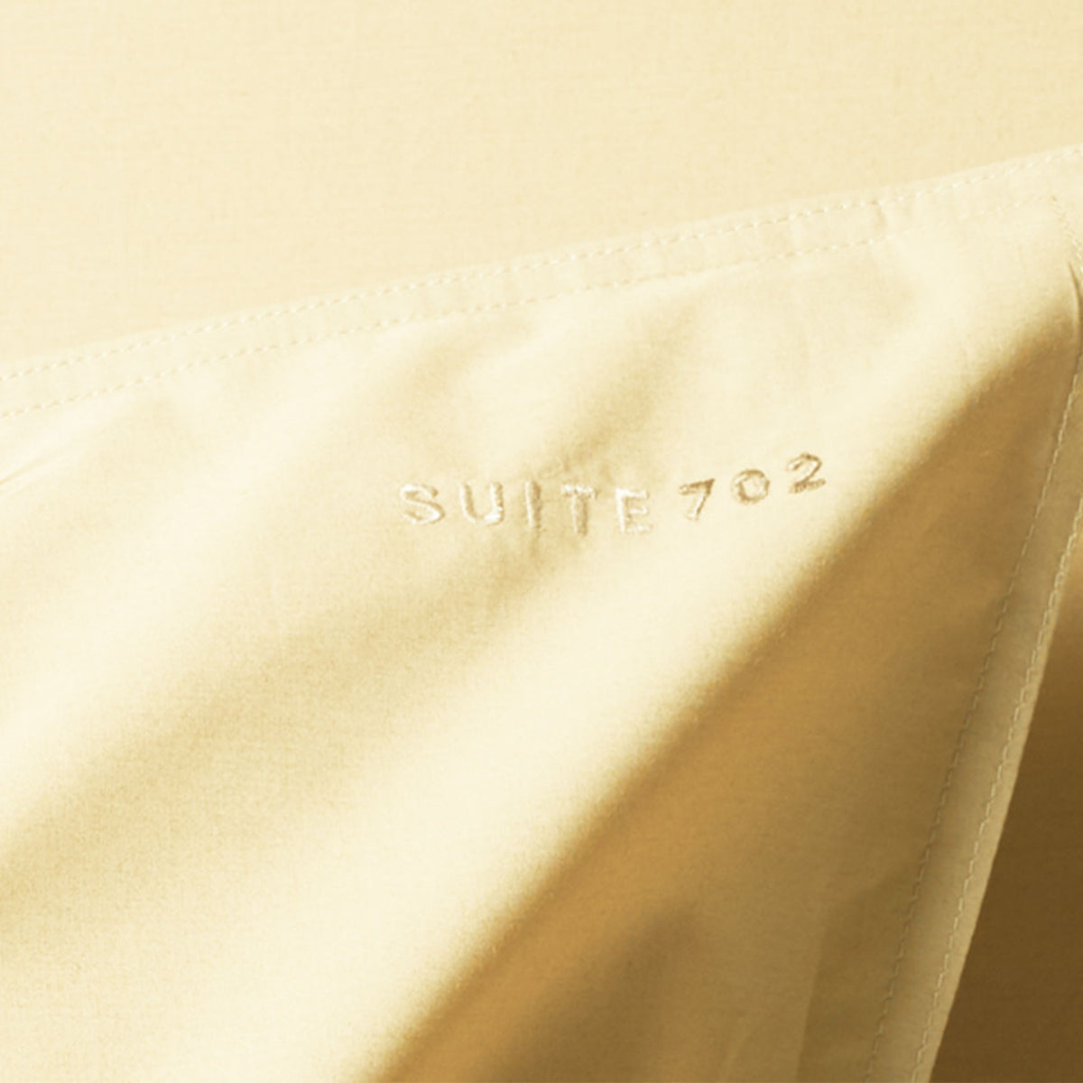 Nahaufnahme des eingestickten „Suite702“-Schriftzugs auf dem Perkal Kissenbezug in Butter Yellow