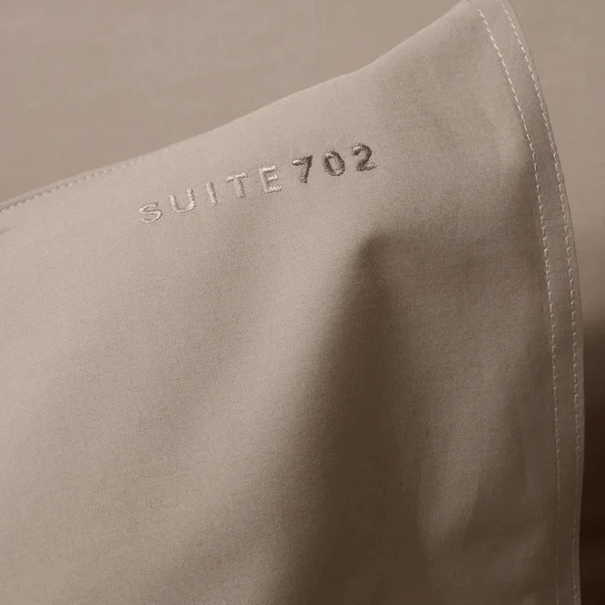 Nahaufnahme der Eckennaht des Suite702 Perkal Kissenbezugs mit gesticktem „Suite702“-Schriftzug, Farbe Camel