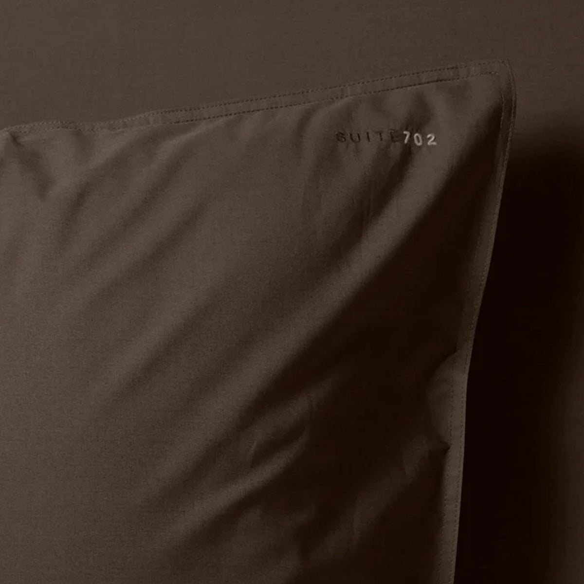 Nahaufnahme der Ecke des Suite702 Perkal-Kissenbezugs in Coffee Brown mit Schriftzug „Suite702“