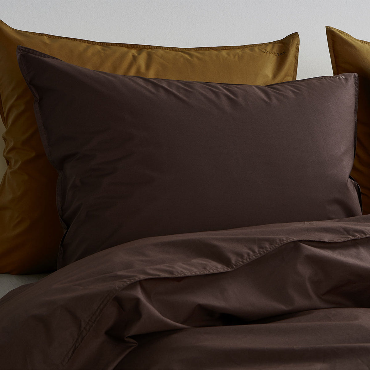 Suite702 Perkal Kissenbezug aus Bio-Baumwolle in Coffee Brown auf Bett mit senfgelben Kissen