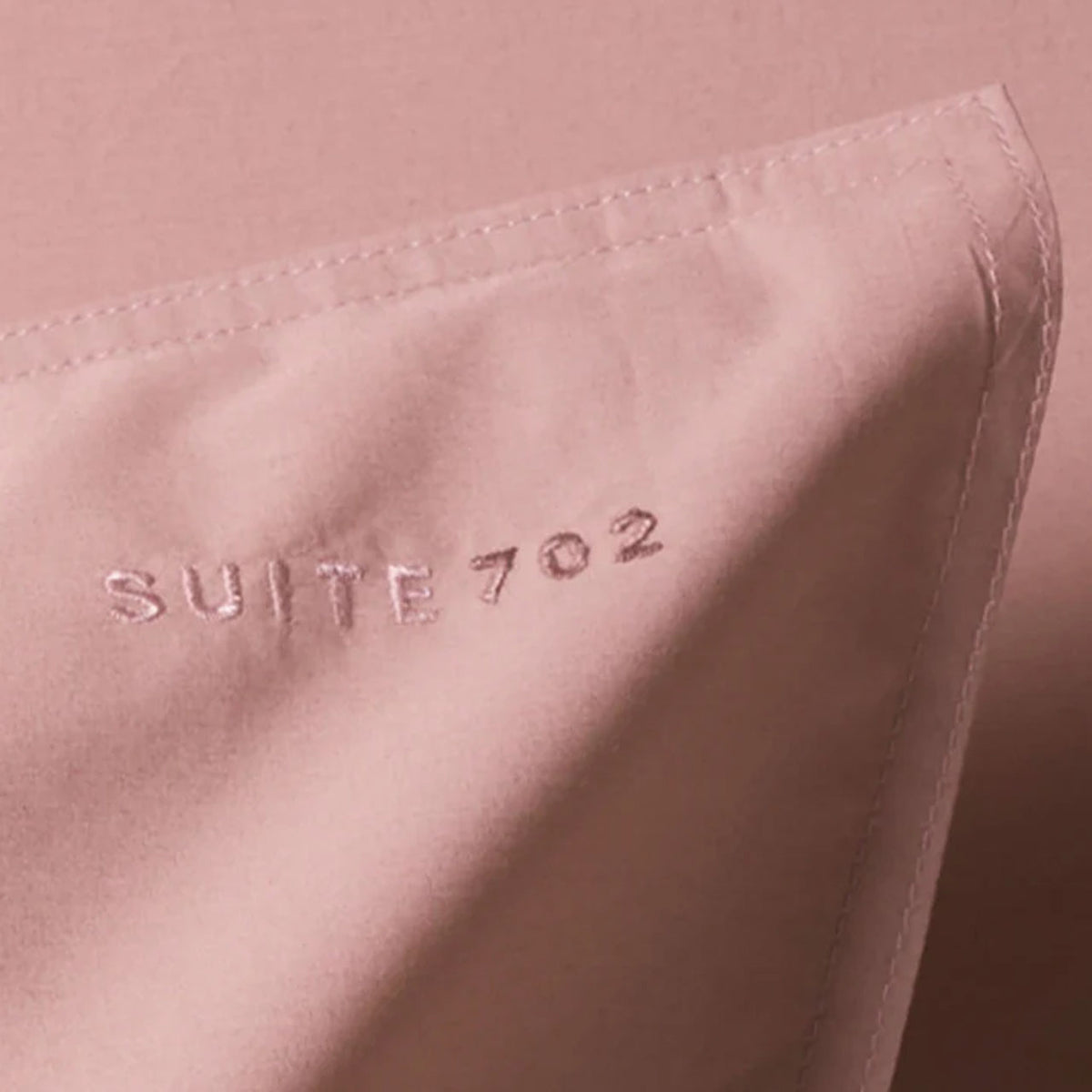 Nahaufnahme der Ecke eines Suite702 Perkal Kissenbezugs mit eingesticktem Schriftzug „Suite 702“, Farbe Dusty Rose