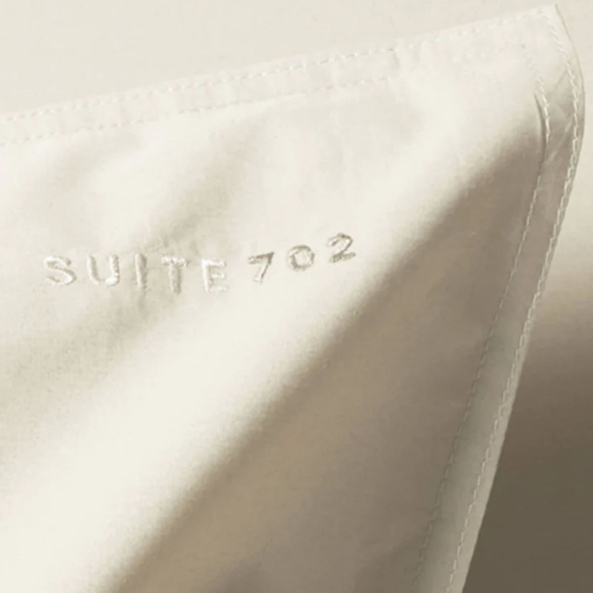 Nahaufnahme der Eckennaht mit eingesticktem „Suite702“-Schriftzug auf Perkal Kissenbezug in Ecru