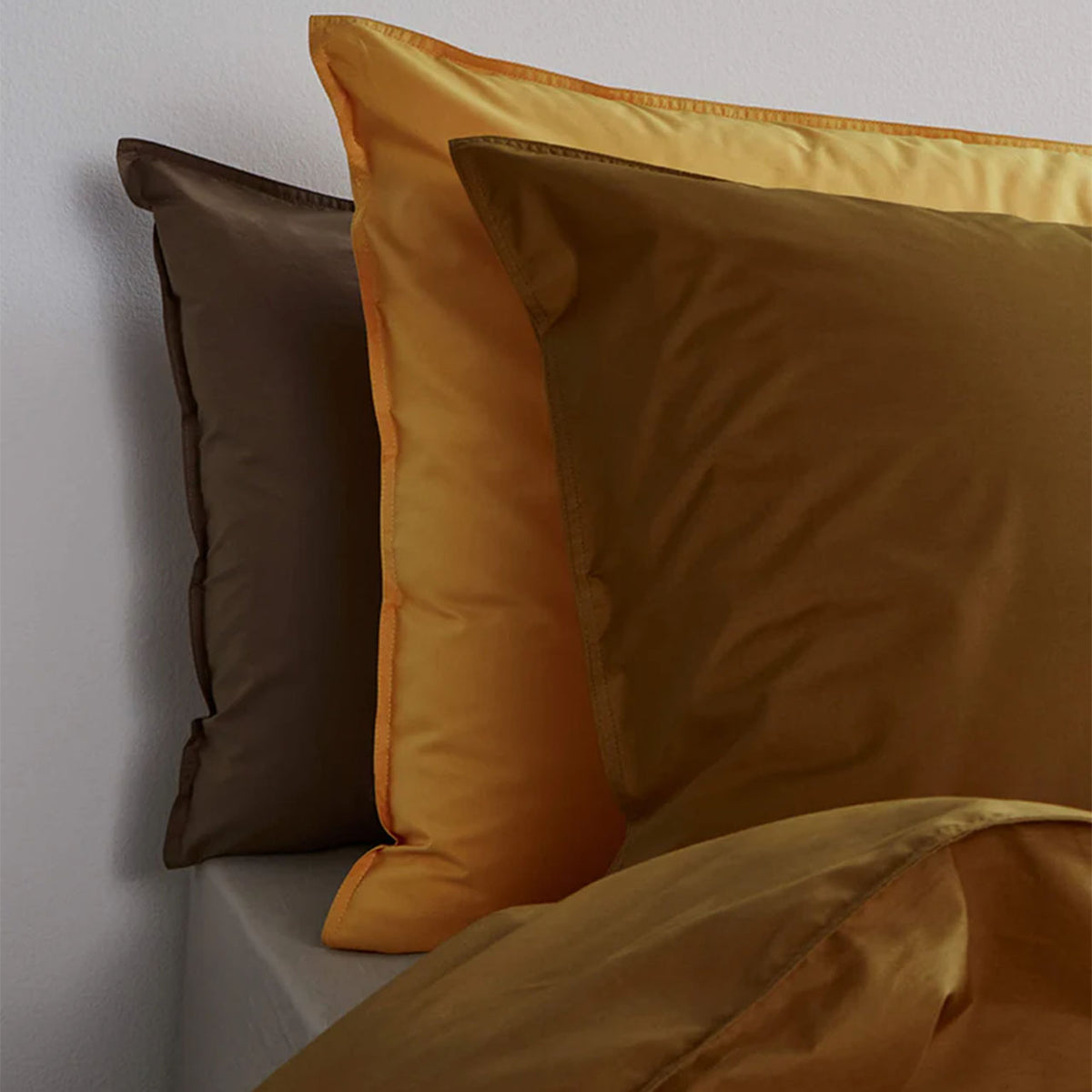 Suite702 Perkal Kissenbezüge aus Bio-Baumwolle in Coffee Brown, Butter Yellow und Khaki Gold, gestapelt im Bett