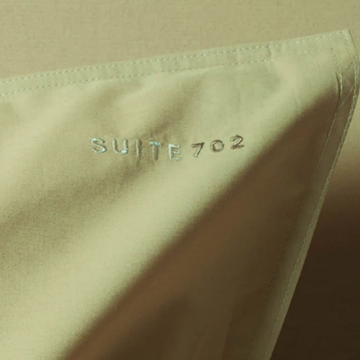 Nahaufnahme der Eckenkante mit eingesticktem „Suite702“-Schriftzug auf dem Perkal Kissenbezug in Camel