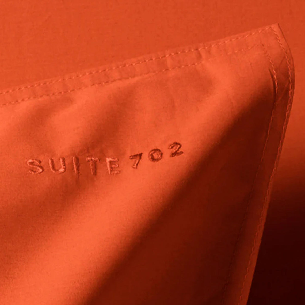 Nahaufnahme der eingestickten Schriftzugs „Suite 702“ auf dem Perkal Kissenbezug in Poppy Orange