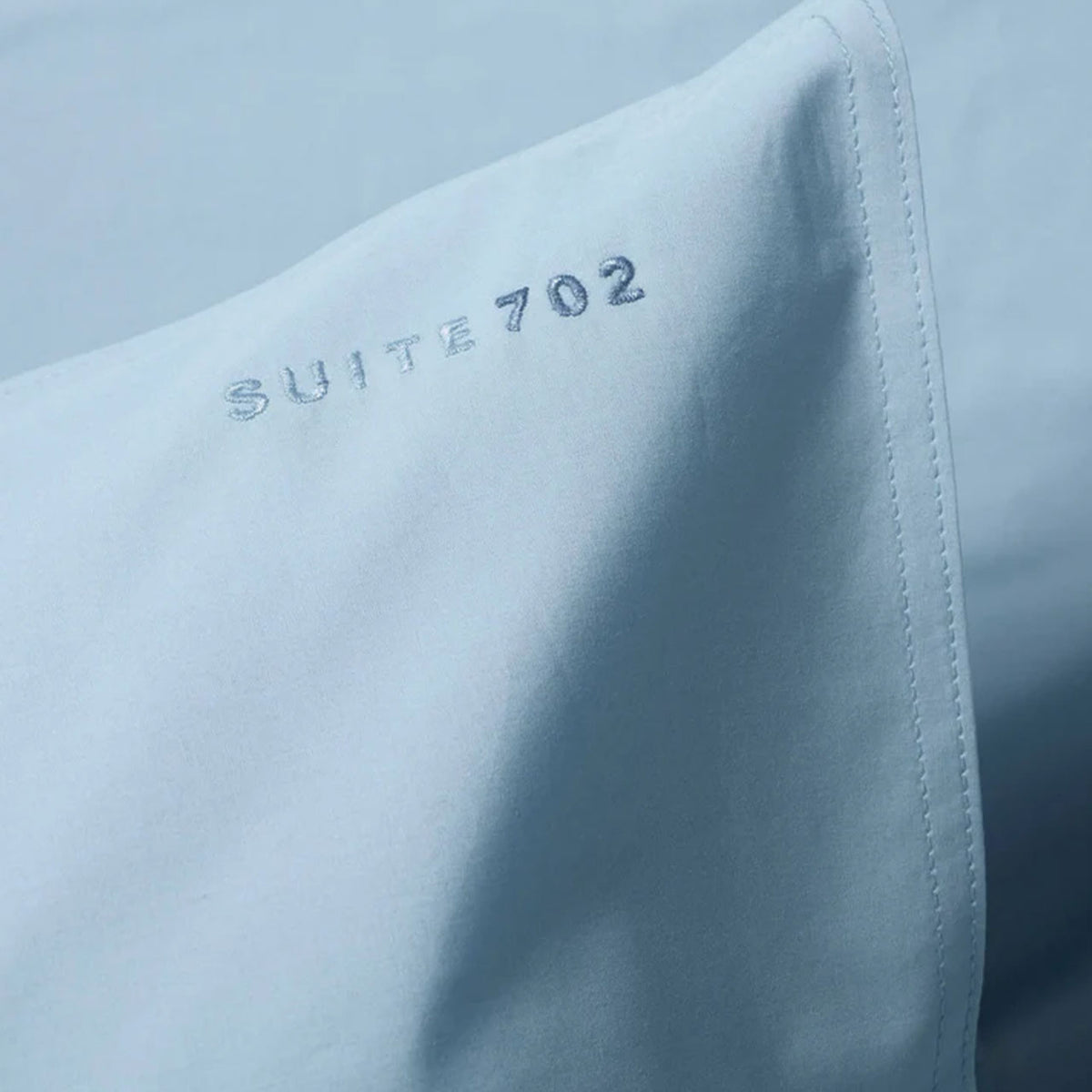 Nahaufnahme der Eckspitze des Suite702 Perkal-Kissenbezugs in Sky Blue mit Schriftzug „Suite702 702“