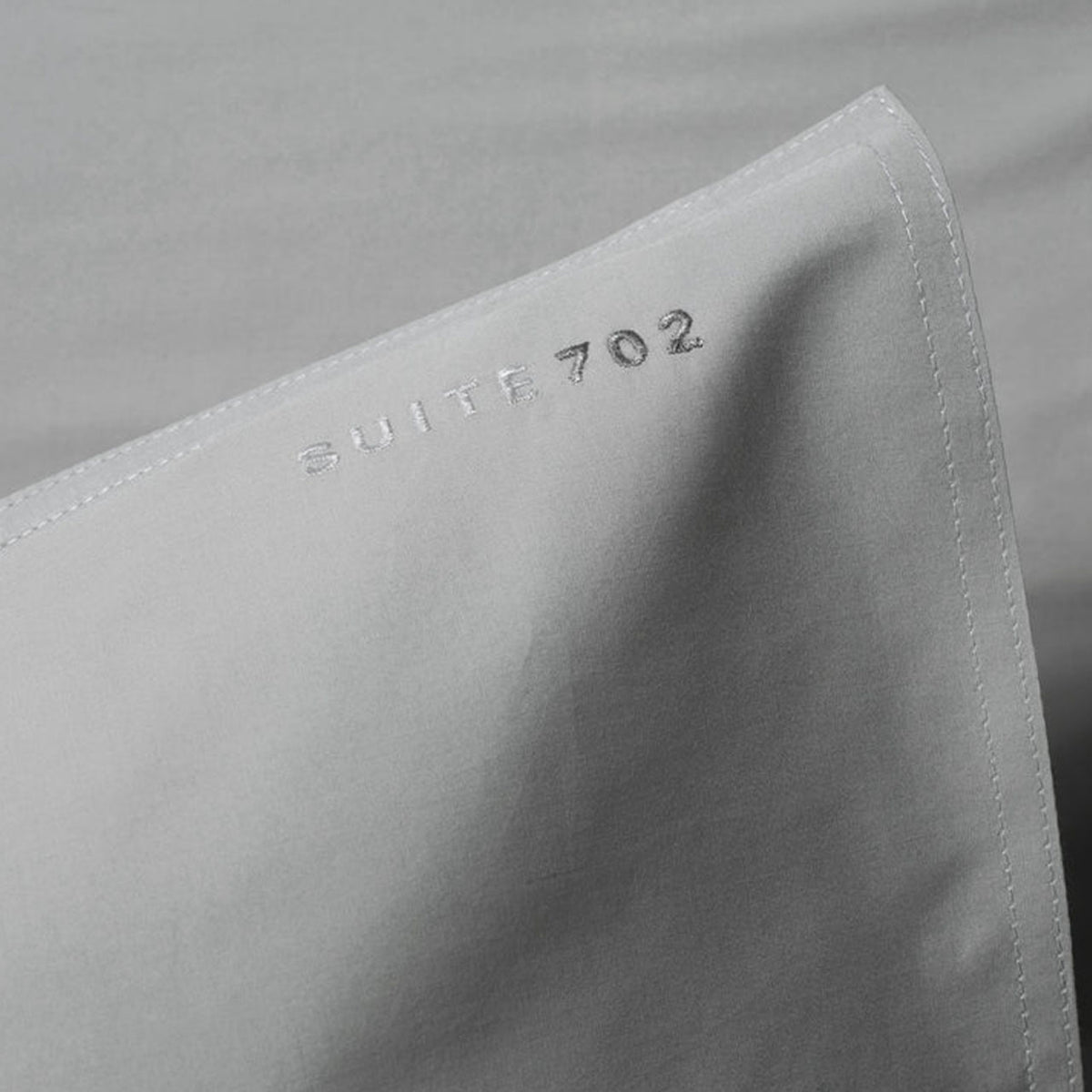 Nahaufnahme der Eckenaht des Suite702 Perkal Kissenbezugs in Urban Grey mit eingesticktem Schriftzug „Suite702“